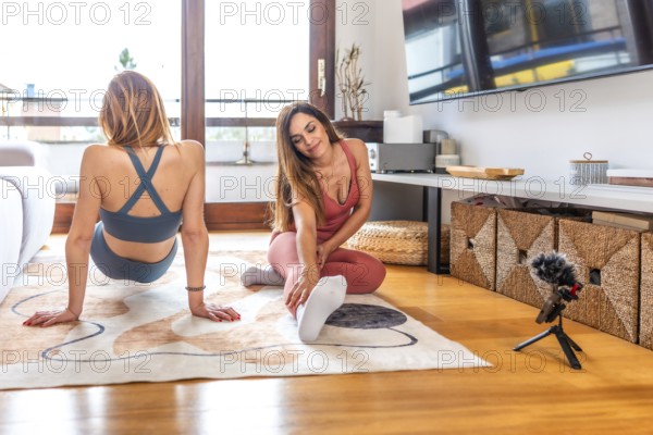 Two women wearing sportswear practicing and recording online yoga class at home in their living room