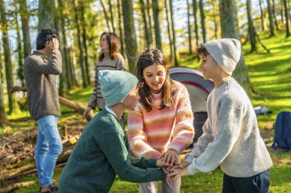 Two caucasian brothers and sister stacking hands playing in the forest enjoying camping with family