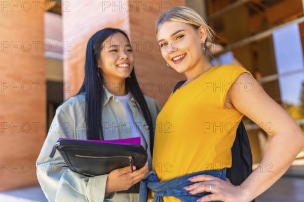 Caucasian and chinese female university students smiling at camera and standing outside the university entrance