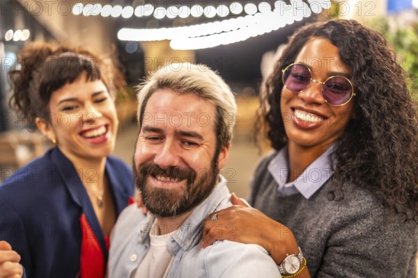 Happy diverse multi-ethnic young friends taking selfie at night party outdoors in a terrace bar