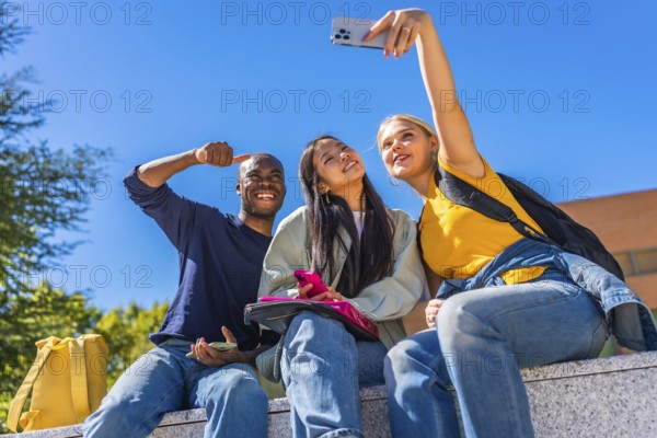 Group of smiling multi-ethnic students taking selfie sitting outside the campus in a sunny day
