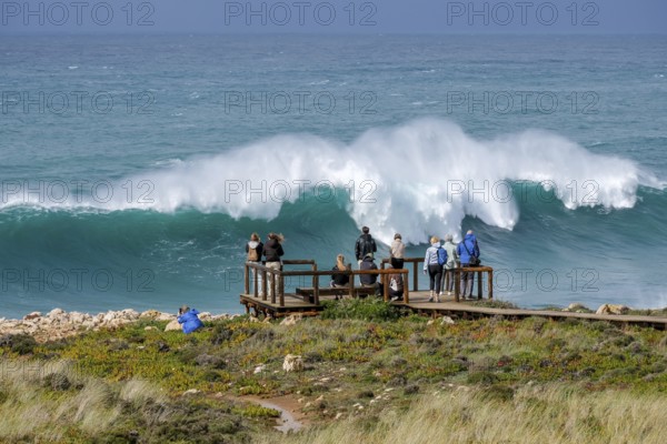 Carrapateira, Algarve, Portugal - Tourists on a viewing platform marvel at the roaring surf and spray not far from Praia do Bordeira on a stormy spring day. Carrapateira is a village in the municipality of Bordeira in the south of Portugal. It is located in the Parque Natural do Sudoeste Alentejano e Costa Vicentina, Southwest Alentejo and Costa Vicentina nature park Park
