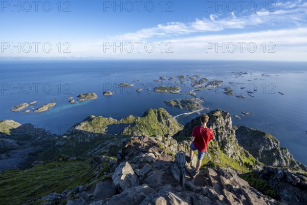 Mountaineer on the summit of Festvagstinden, view of the sea and archipelago islands with the village of Henningsvær, coastal landscape, Lofoten, Nordland, Norway, Europe
