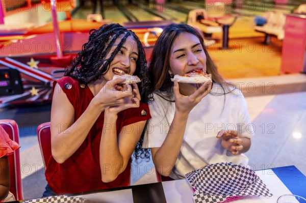 Two joyful young women sharing delicious pizza while enjoying a fun filled day at the bowling alley, creating lasting memories together