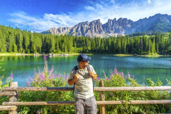Hiker admiring the stunning scenery of lake carezza with the latemar mountain range in the background, dolomites, italy
