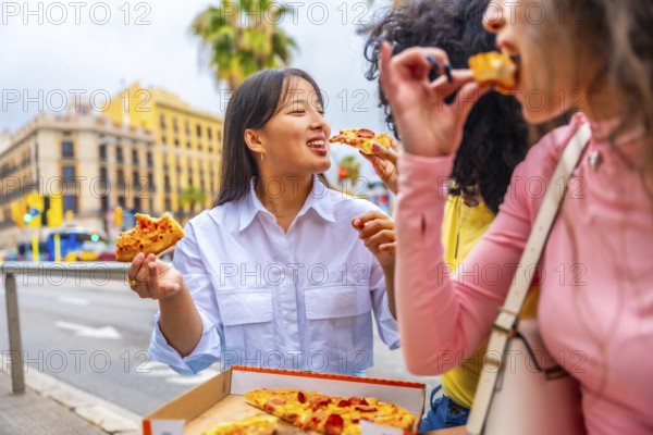 Three multicultural female friends sharing and eating pizza sitting outside