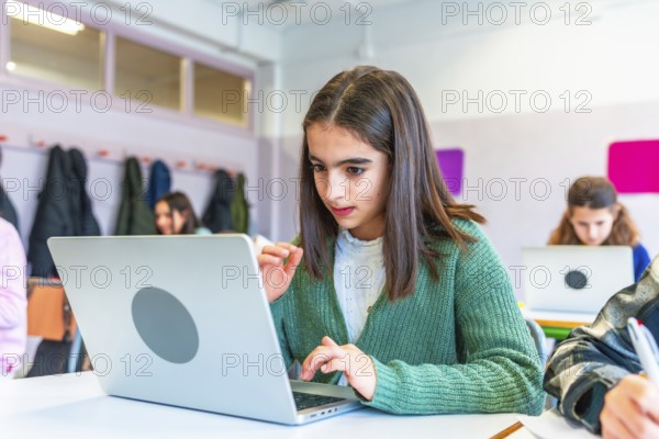 Schoolgirl concentrating on her laptop during a lesson, surrounded by classmates in a modern classroom