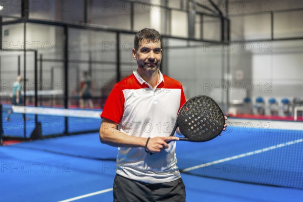 Portrait of a sportive mature man with paddle tennis racket standing in a blue indoor paddle court