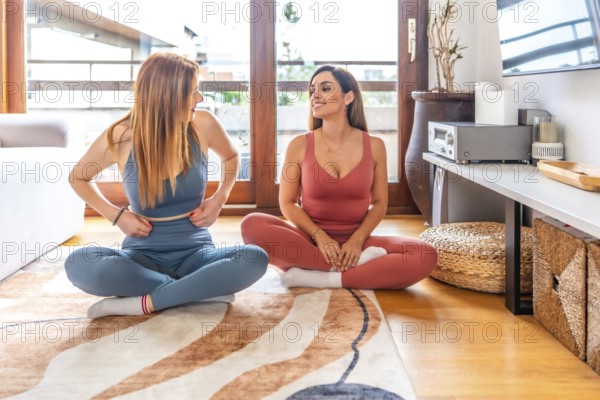 Two friends engaging in yoga and meditation at home, participating in an online class in a bright, modern living room setting