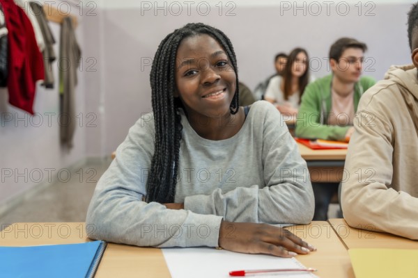 Young black female student is smiling while sitting at her desk in a classroom during a lesson with her classmates