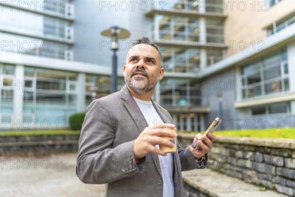 Mature caucasian businessman using phone during coffee break outside the office enjoying fresh air