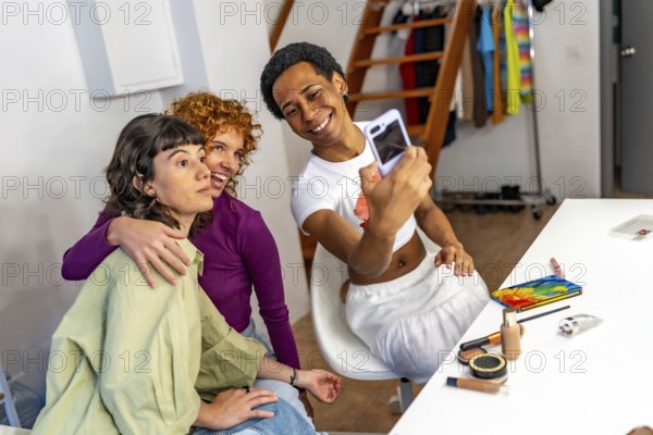 Non binary person and gay friends taking selfie while making up at home