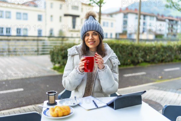 Happy beauty woman enjoying warm tea working with tablet in an outdoor sidewalk cafeteria