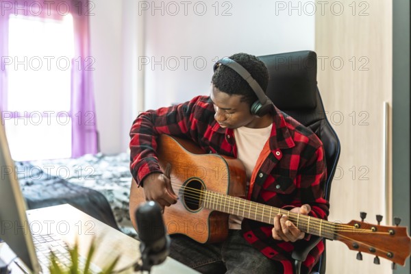 Young man playing acoustic guitar and recording music using a computer and microphone at home