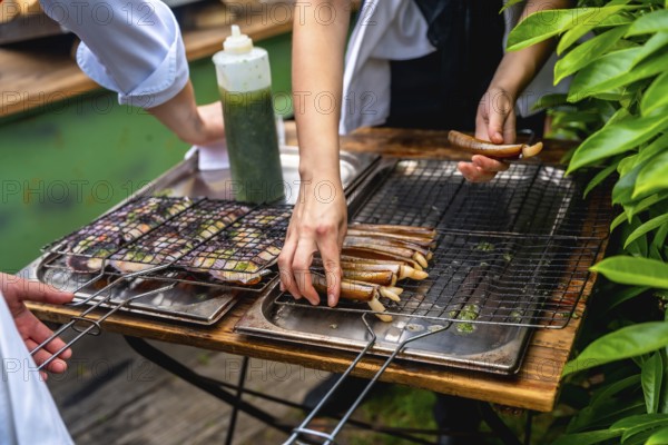 Chefs grilling seafood in an outdoor setting, preparing dishes for a wedding reception, with fresh ingredients and greenery surrounding the area