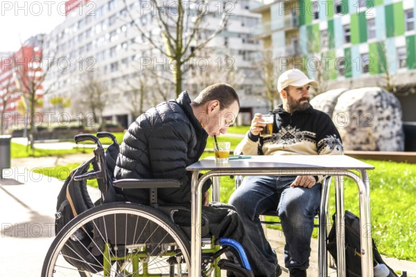 Two men enjoy drinks at an outdoor cafe, one using a wheelchair, demonstrating inclusivity and friendship