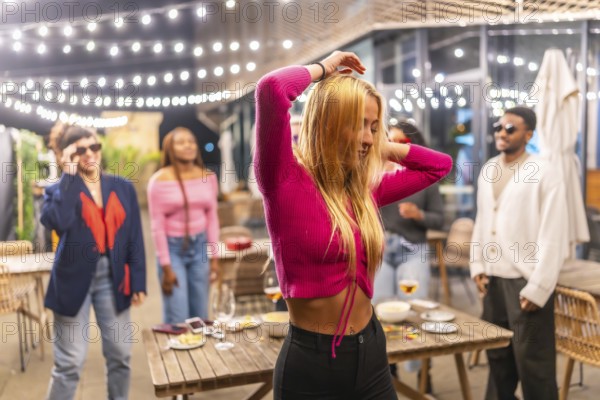 Blonde sensual woman dancing with friends at night party at the terrace of a bar decorated with lights