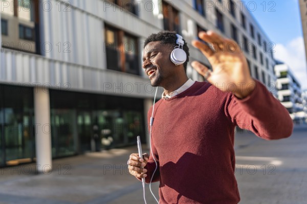 Energetic african young man listening to music and dancing while walking along a city street