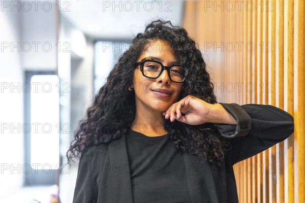 Portrait of a confident and cheerful latin businesswoman with long curly hair and formal elegant clothes smiling at camera standing inside a modern financial building