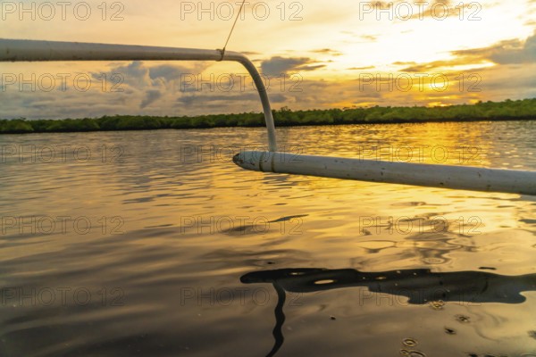 Outrigger of a banca boat sailing on calm water during a golden sunset in siargao island, philippines