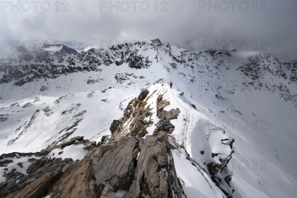 Mountaineer descending the narrow ridge of Piz Laviner, view of mountain panorama in wintry mountain landscape with dramatic clouds, Grisons Haute Route, Albula Alps, Rhaetian Alps, Grisons, Eastern Switzerland, Switzerland, Europe