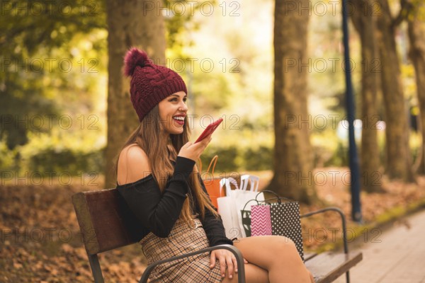 Portrait of a woman in autumn in a forest with brown leaves walking with paper bags after shopping sitting in the park
