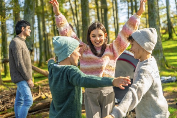 Brothers and sister raising hands after stacking while enjoying a camping day with family in a green alpine forest