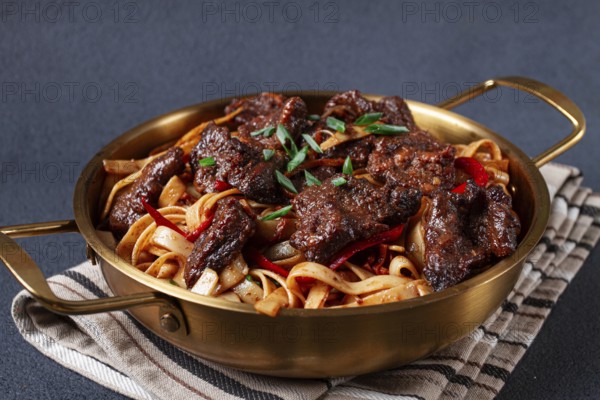 Udon noodles with Mongolian beef, green onions and vegetables, in a brass pan, on a gray background, homemade, no people