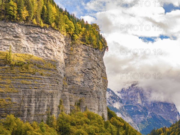 Steep rock face with autumn-coloured forest at the foot and partly cloudy sky, Switzerland, Europe