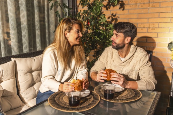 Young couple enjoying a cozy meal and drinks on their balcony, soaking in the warm summer evening and sharing laughter during sunset