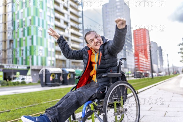 Portrait of a cheerful disabled man raising his arms in celebration, sitting in his wheelchair on a city sidewalk