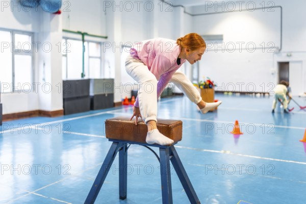 Girl practicing gymnastics, balancing on pommel horse in school gym, showing determination and athleticism during physical education class