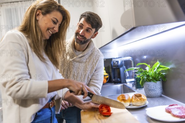 Young couple preparing dinner together, slicing tomatoes and making hamburgers in their modern kitchen