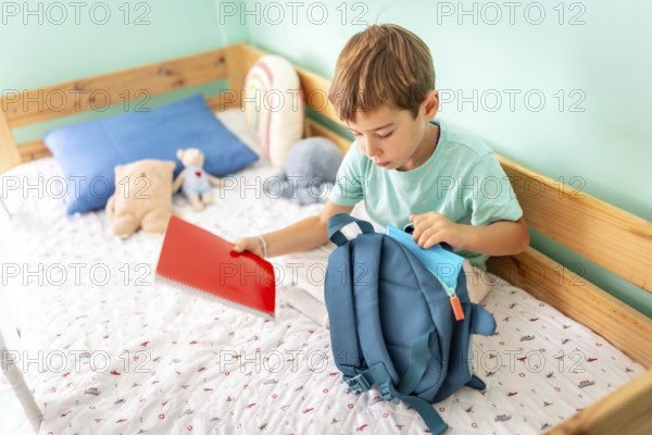 Schoolboy prepares his backpack for school sitting on bedroom and preparing for school