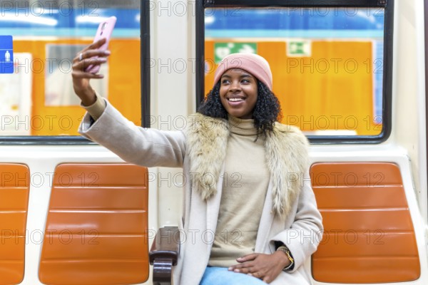 Smiling young woman wearing winter clothes taking a selfie while traveling on subway train