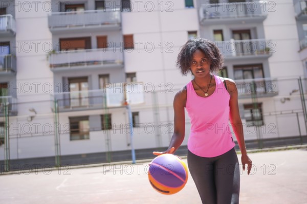 Confident afro woman looking at camera while dribbling in an urban basketball court