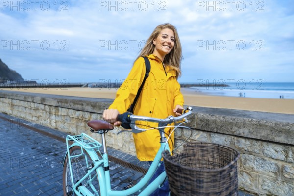 Happy young woman walking with her bicycle on the boardwalk by the beach, enjoying the fresh air and ocean view