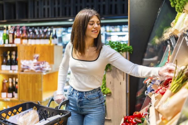 Young woman shopping for groceries, choosing fresh organic vegetables from a display shelf in a supermarket
