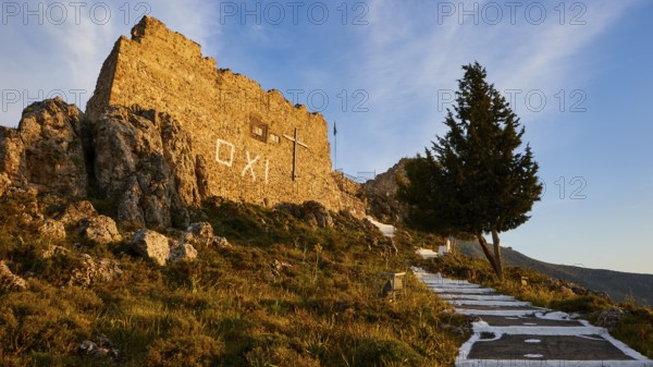 Warm evening light, stone wall of a ruin next to a tree under a blue sky with OXI lettering, Archangelos, castle, place, Castle of Archangelos, Rhodes, Dodecanese, Greek Islands, Greece, Europe