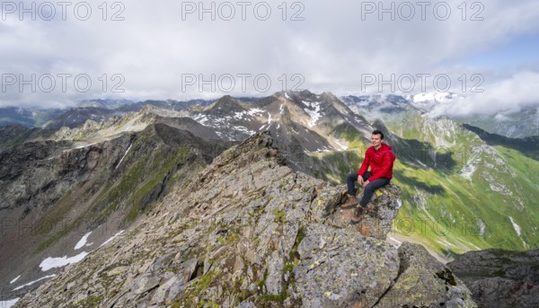 Mountaineer sitting on a rock, on a steep rocky ridge, on the summit of the Lasörling, view of the mountain panorama of the Venediger Group, Lasörling Group, Hohe Tauern National Park, East Tyrol, Tyrol, Austria, Europe