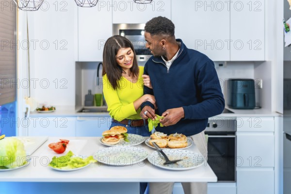 Young multiethnic couple enjoying quality time together while preparing delicious burgers in their stylish modern kitchen