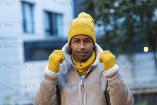 Stylish man wearing a bright yellow hat, gloves, and scarf, braving the cold winter weather while enjoying the vibrant city atmosphere
