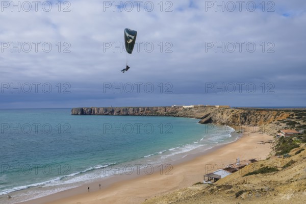 Sagres, Algarve, Portugal - Paraglider flying on the town beach Praia da Mareta, behind the sea fortress Sagres, Fortaleza de Sagres