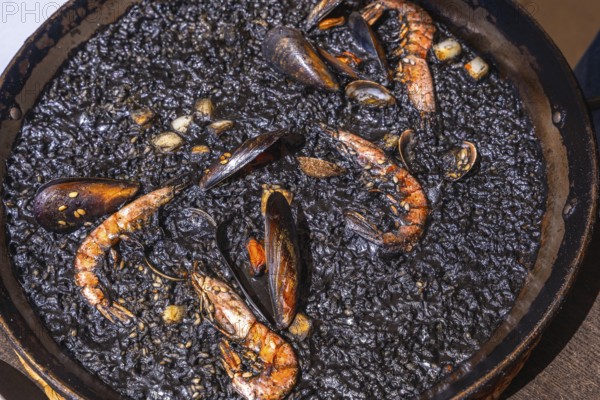 Close up of black paella with shrimps, mussels and other seafood, cooked and ready to be served in a traditional paella pan