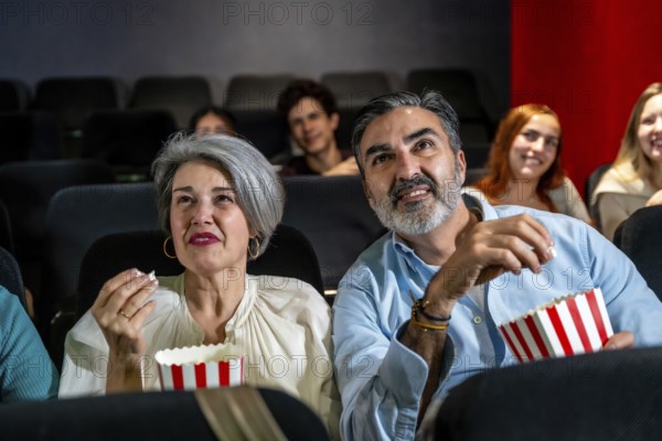 Senior couple watching a movie and eating popcorn, enjoying a night out at the cinema with other people