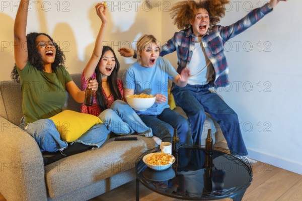 Group of young multi ethnic people enjoying a sports event on television, drinking beer and eating chips
