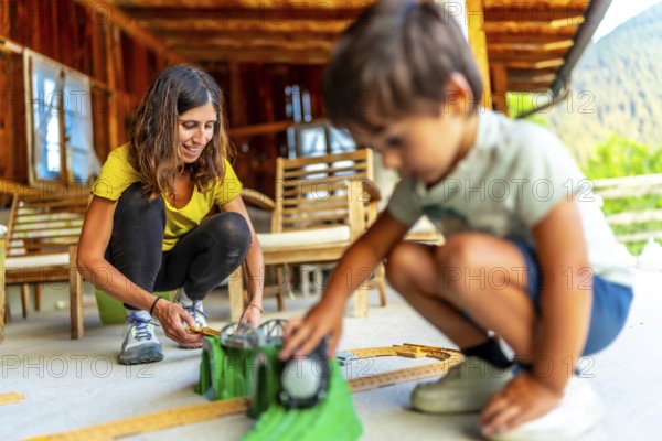 Mother and son enjoying quality time together, building toy train tracks on a porch