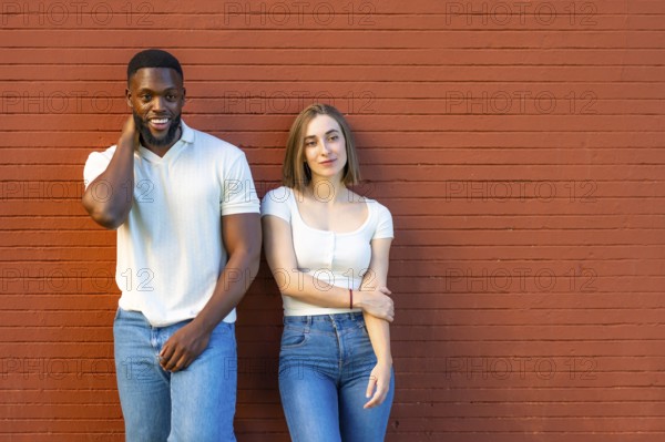 Horizontal photo with copy space of a shy multi-ethnic couple in denim clothes leaning on urban wall together