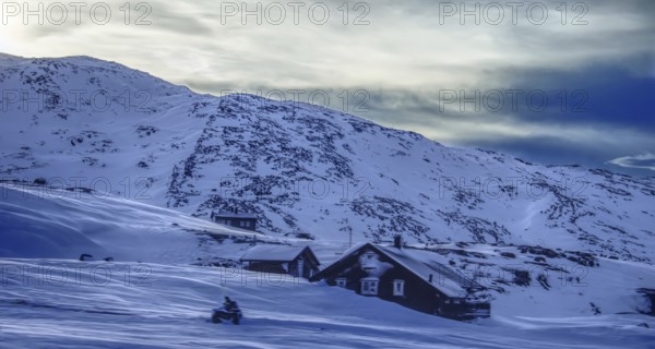 Snow-covered landscape with individual houses against a mountain backdrop in the morning light