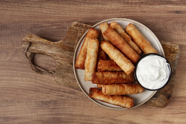 Fried spring rolls with cheese, on a wooden background, with cream sauce, no people